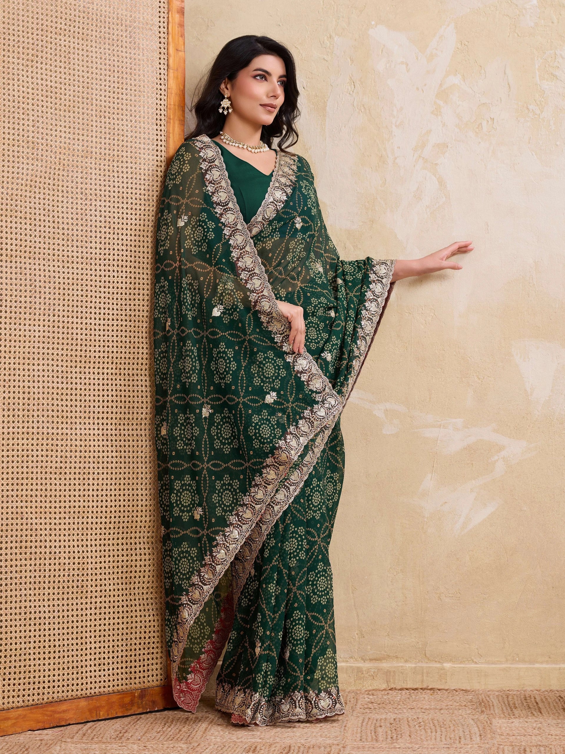 Woman wearing a green saree with silver border against a textured beige wall.